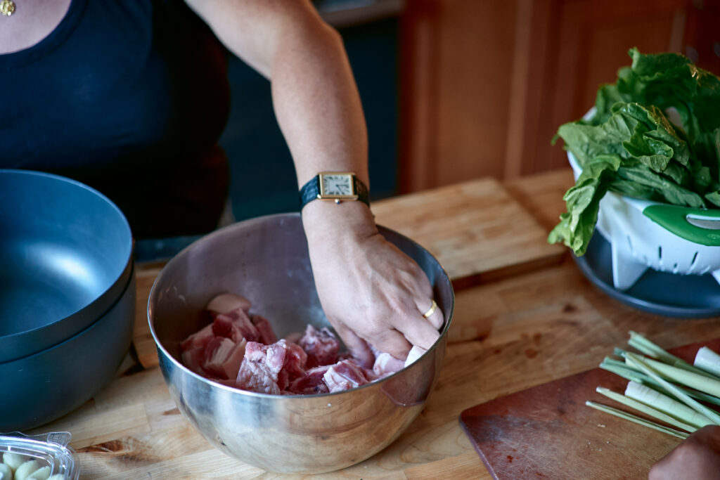 Hand with watch on wrist stirs raw pork in metal bowl. 