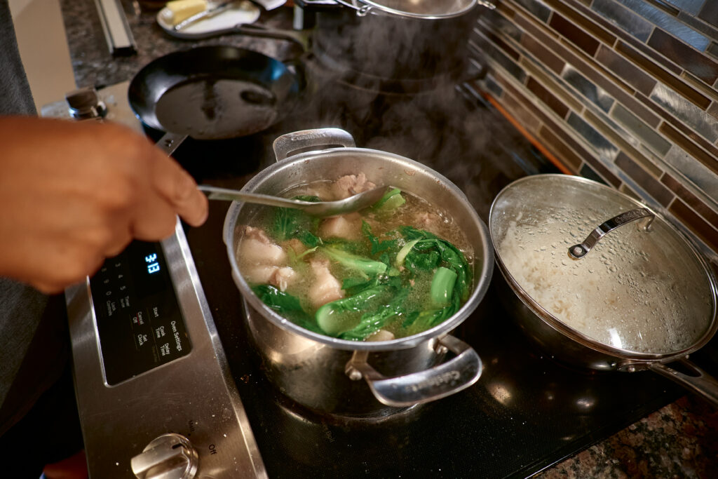 Hand stirs pot on stove containing pork and greens.