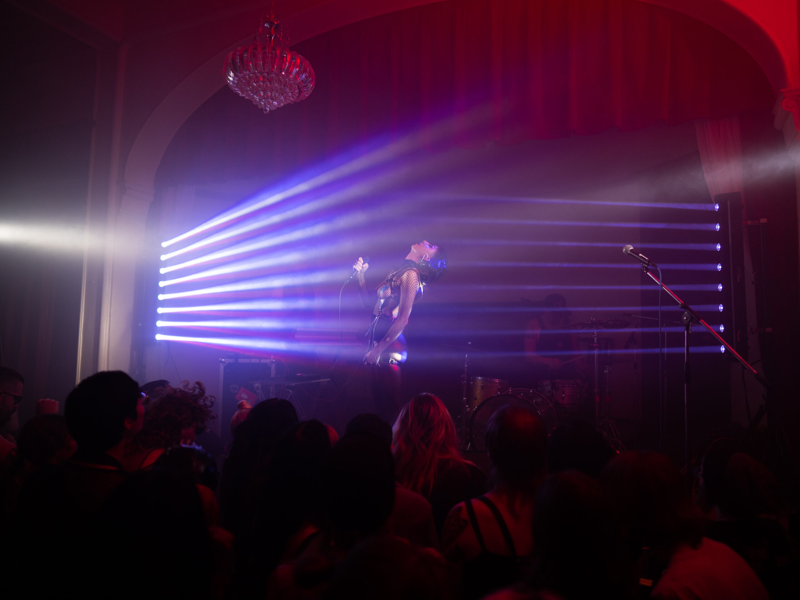 Performer holds microphone and faces beams of purple light.