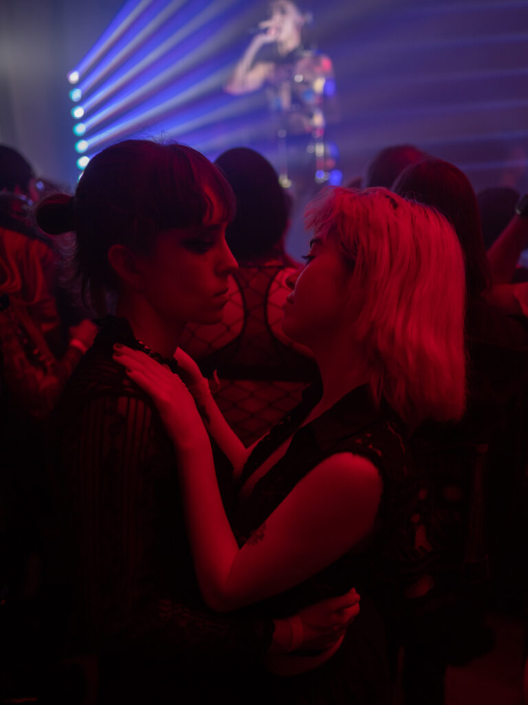 Two people gaze at each other on the dance floor, bathed in red and purple light.
