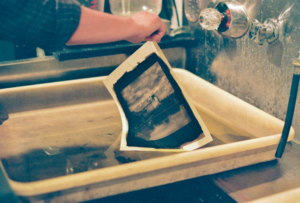 Hand picks up freshly developed, still wet photograph from tray.