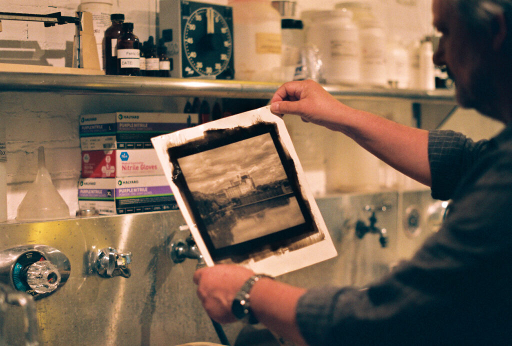 Person holds up freshly developed photograph in darkroom.