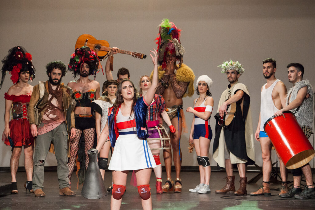 Performer gestures holding megaphone in front of ensemble of actors standing in a line.