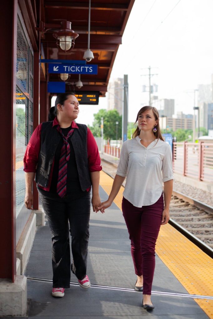 Two performers hold hands and walk down platform at lightrail station.