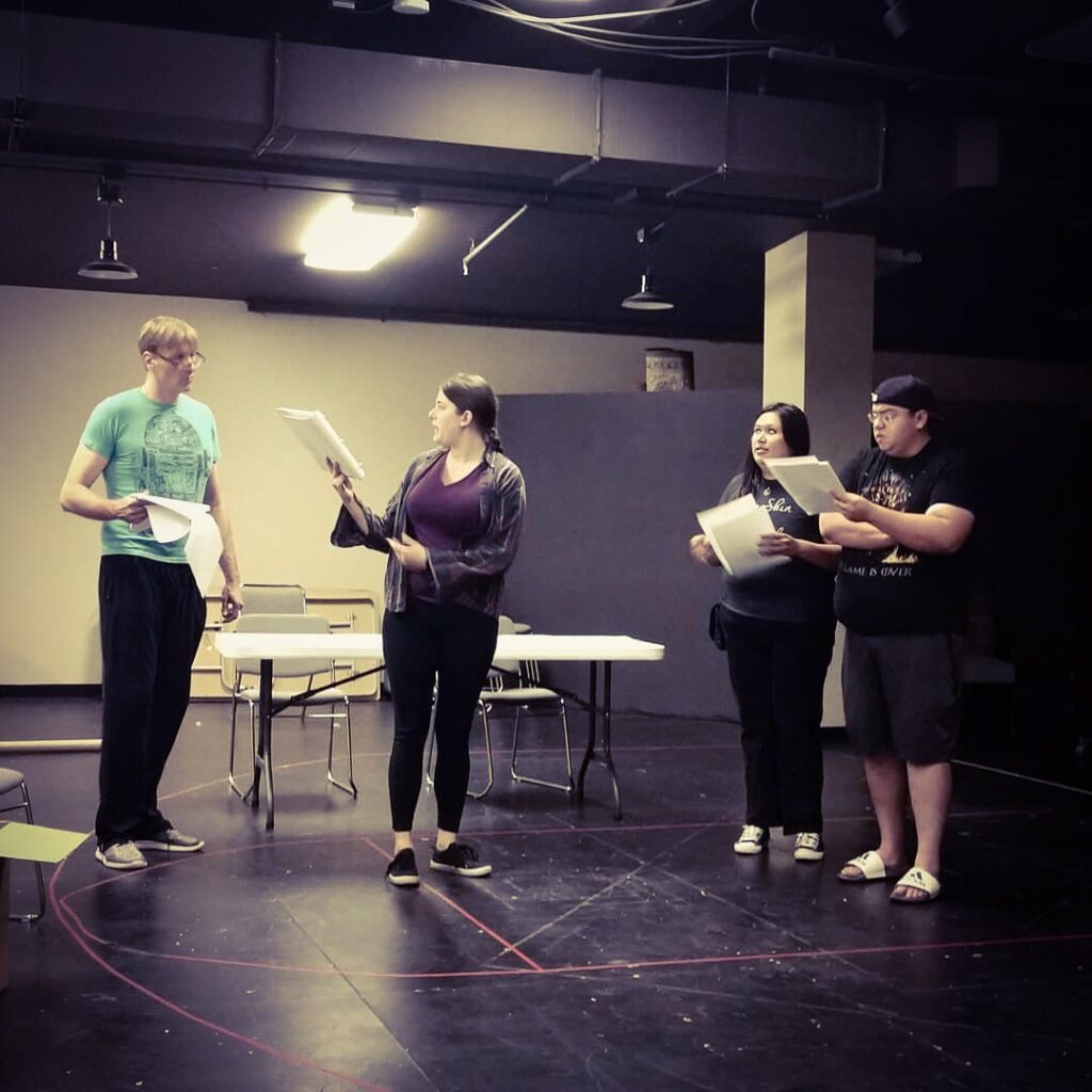 Four actors rehearse holding scripts.