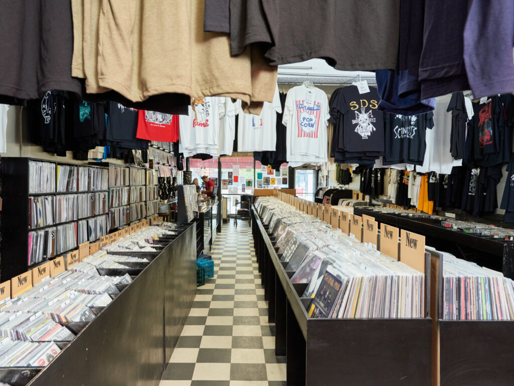Aisle of record store with black and white tile floor and hanging t-shirts.
