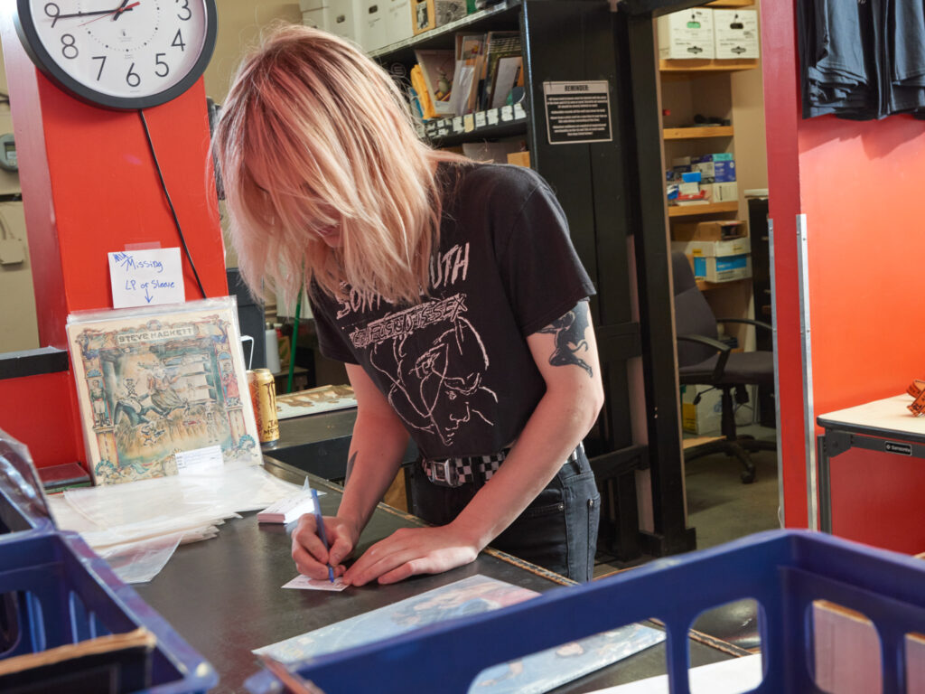 Person with blonde hair writes on counter of record store.