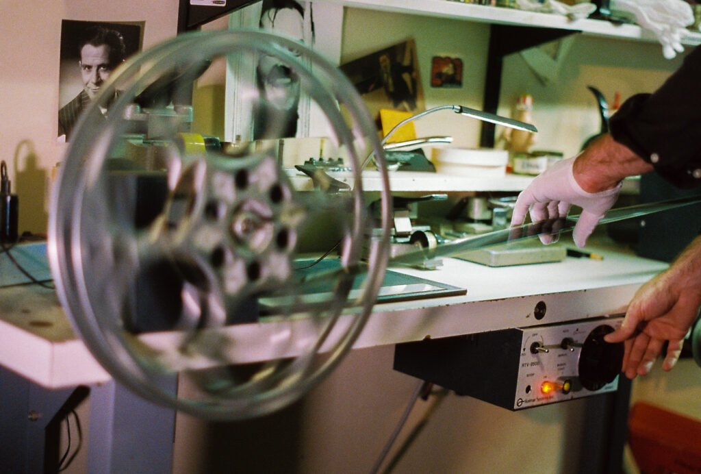 Hand in white glove feeds film reel onto spool, with shelf in background.