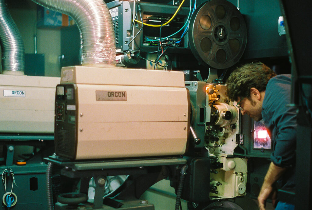 Person bends to examine beige Orcon film projector.
