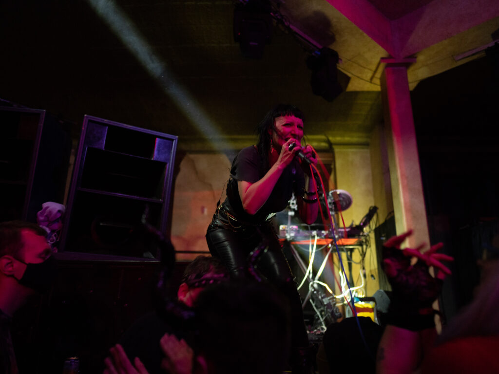 Performer onstage crouches to sing into microphone, with green light behind them.