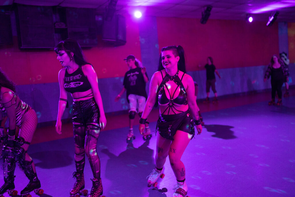 Roller skaters smile dressed in black, on rink with purple light.