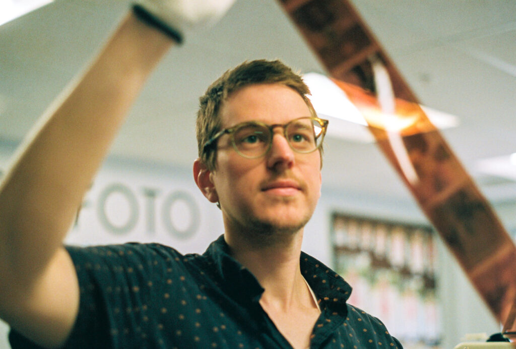 Person with light skin and glasses holds up film strip to light.