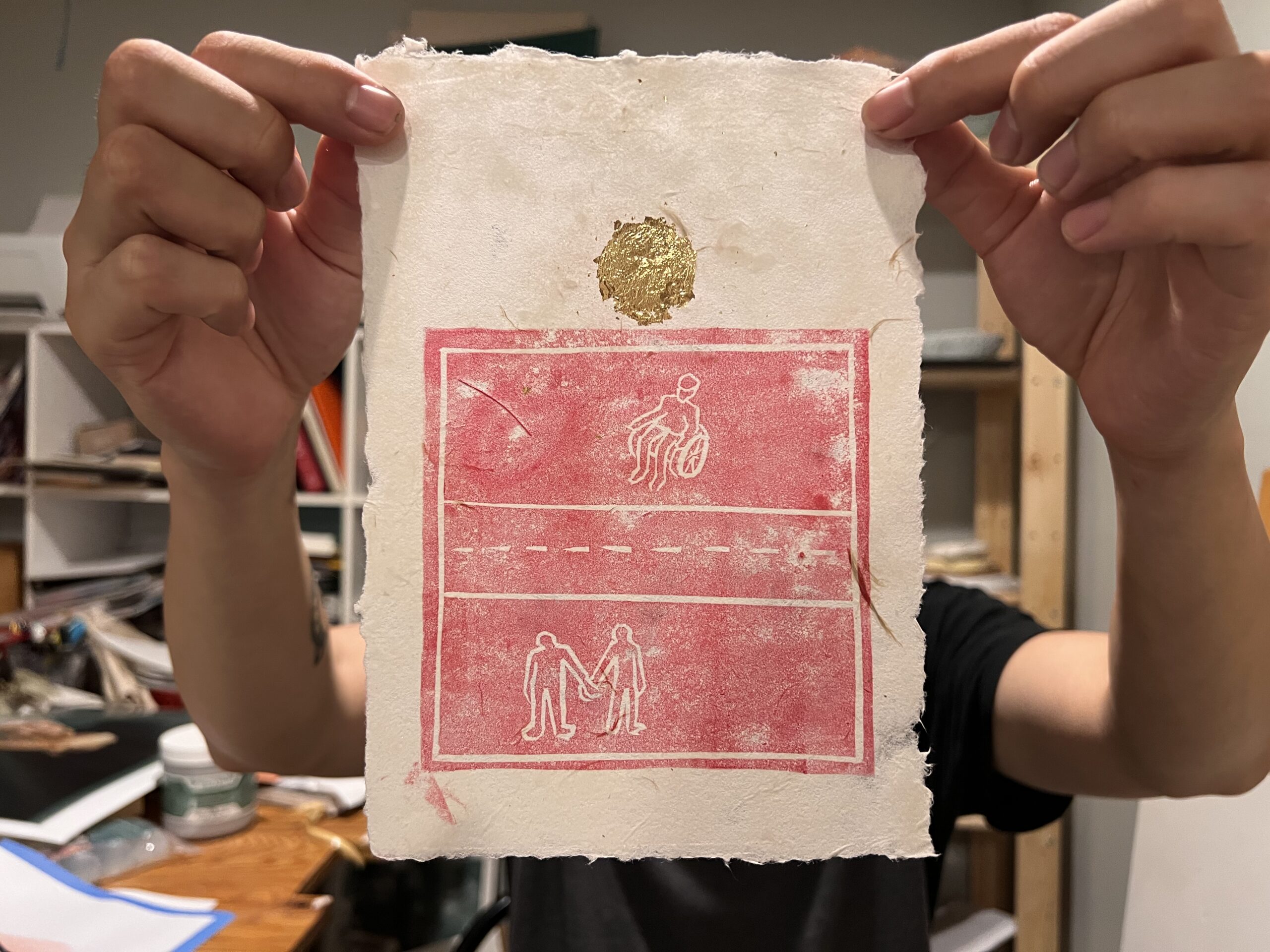 Hands holding up print with red design and gold seal above.