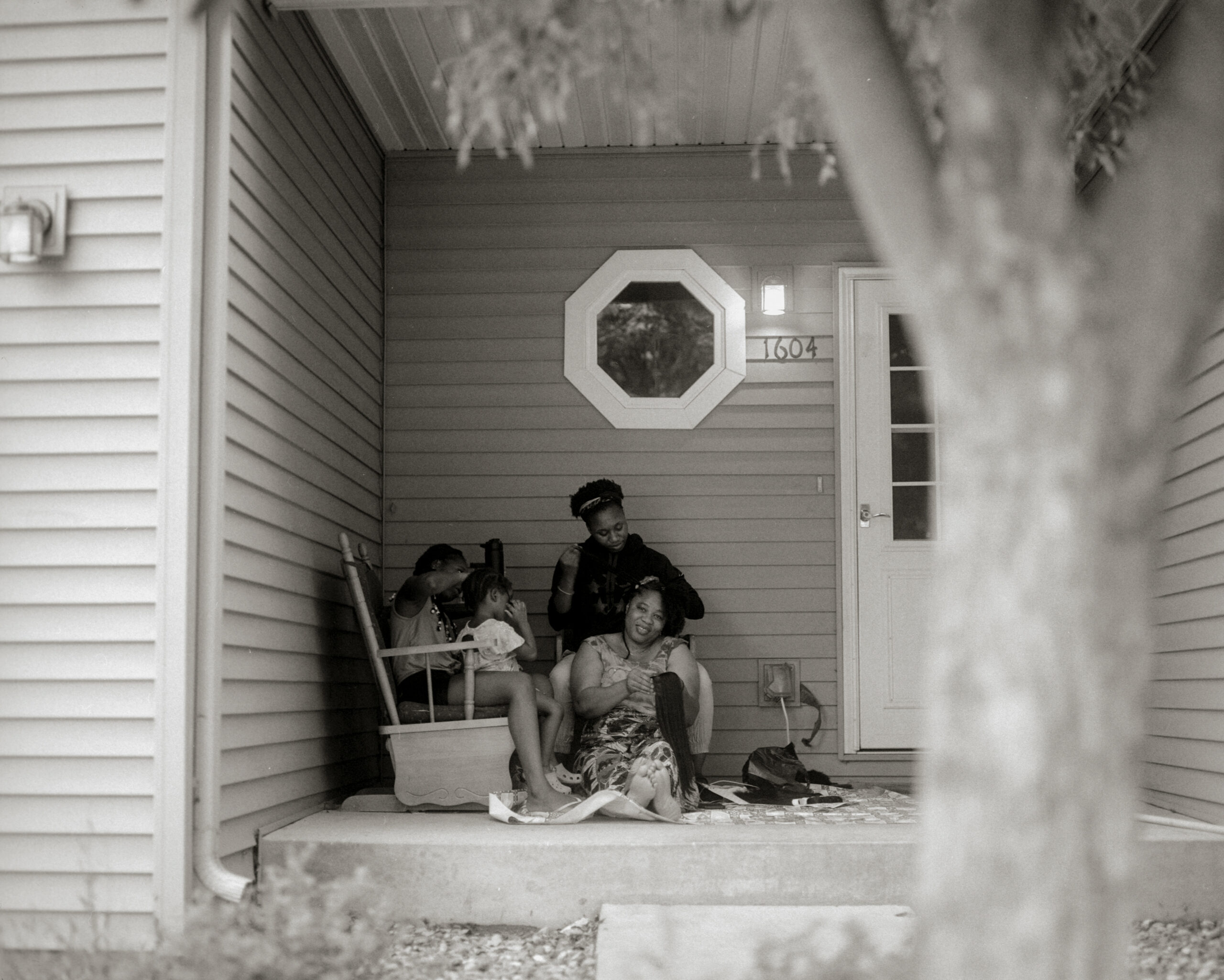 Black women and girls braid hair on front porch.