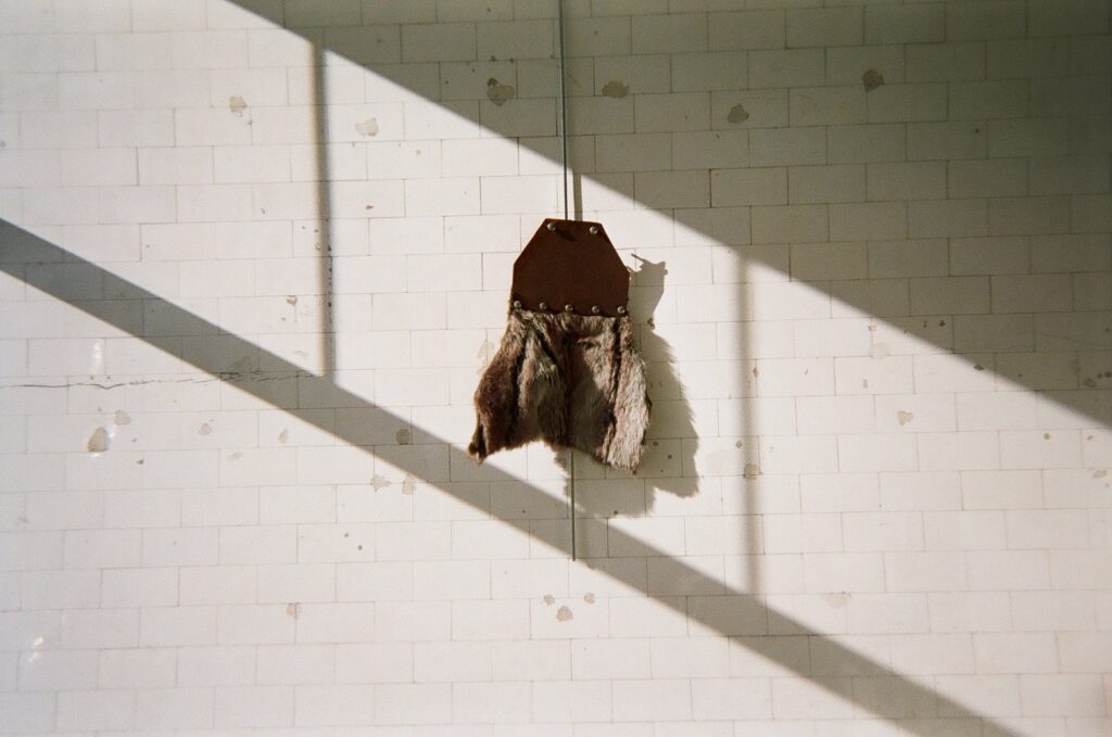 Form with brown fur, leather, and grommets hangs against white wall with sunlight and shadows.