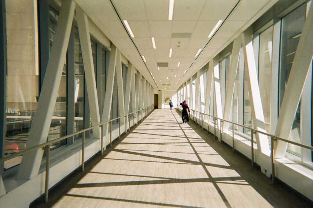 Two people walk down skyway, with white beams and sunlight.