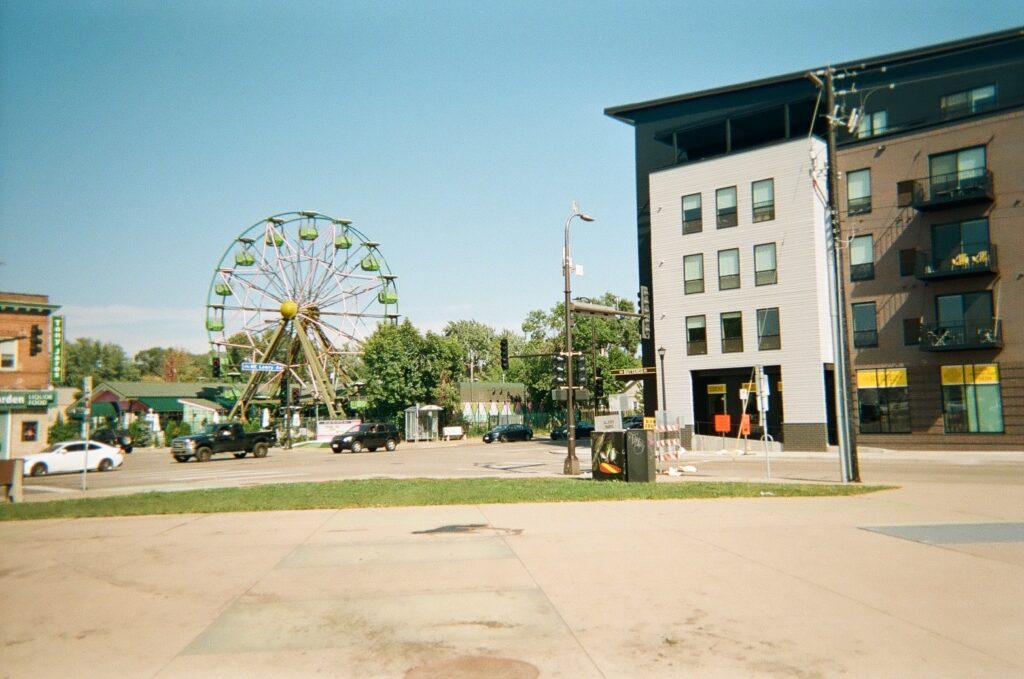 Intersection of city streets with condo building at right and ferris wheel in background.