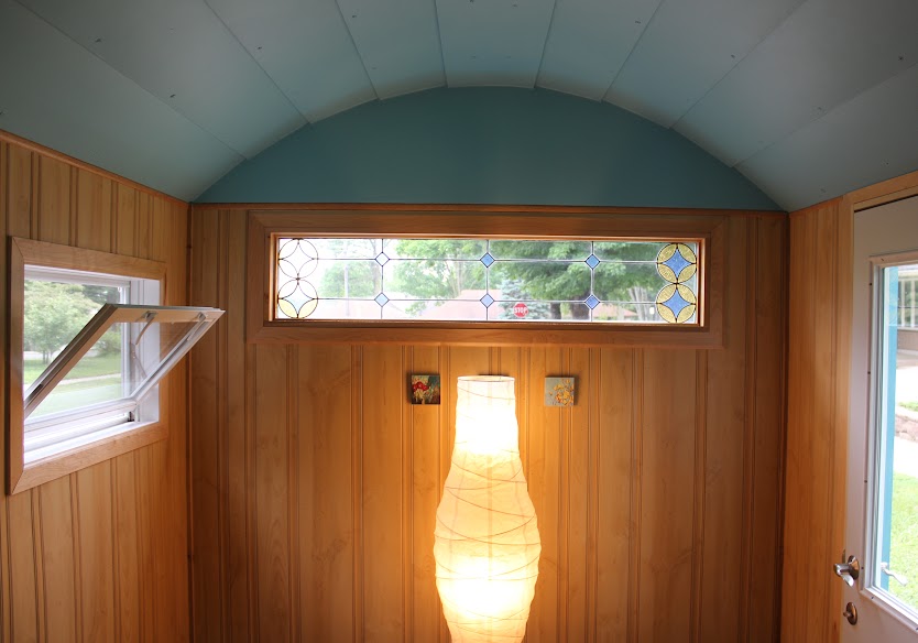Interior of a trailer with a domed turquoise roof, wood panelling, and a stained glass window.