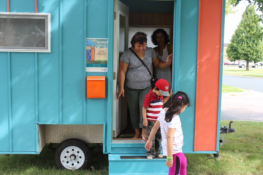 Two women and two children exiting a trailer painted turquoise with a pink stripe and orange mailbox.
