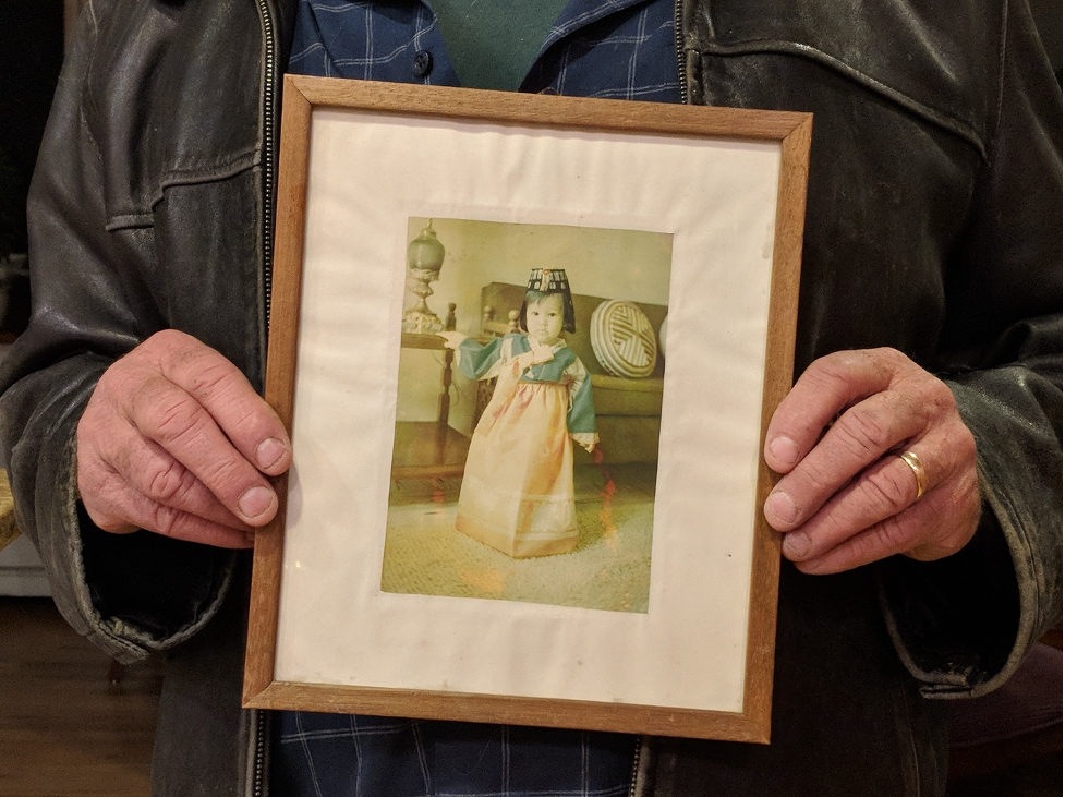 Hands hold wood-framed portrait of child in hanbok dress.