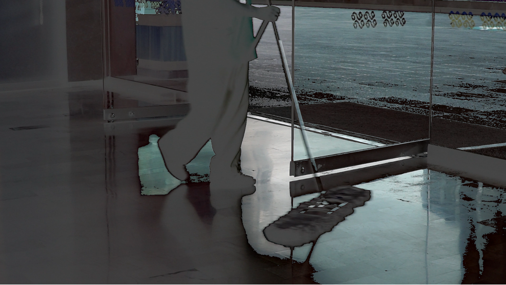 Feet of person pushing dry mop on shiny floor, with glass door behind.