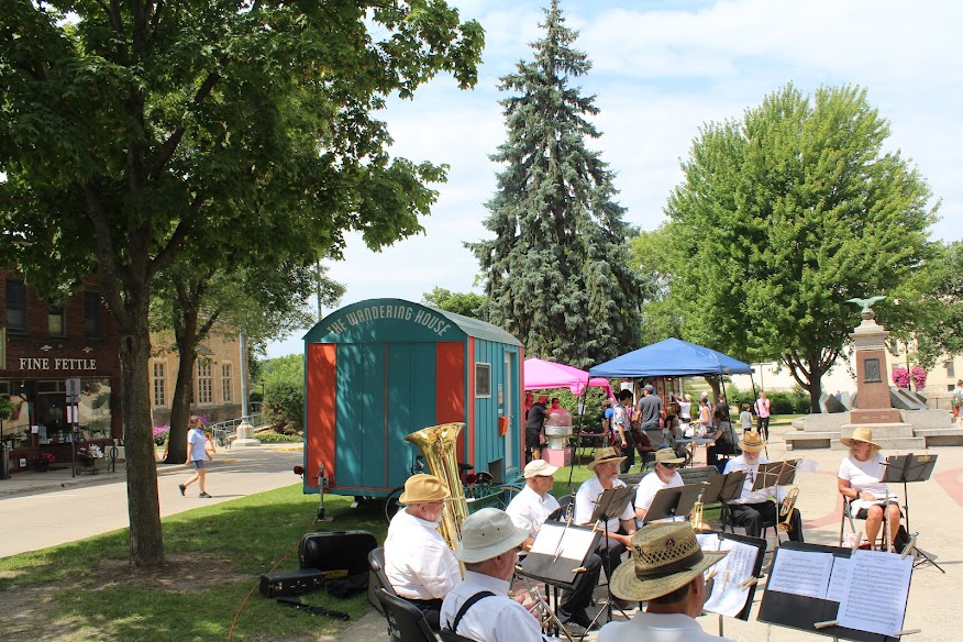 Town square in summer with turquoise and pink trailer and musicians playing in foreground.