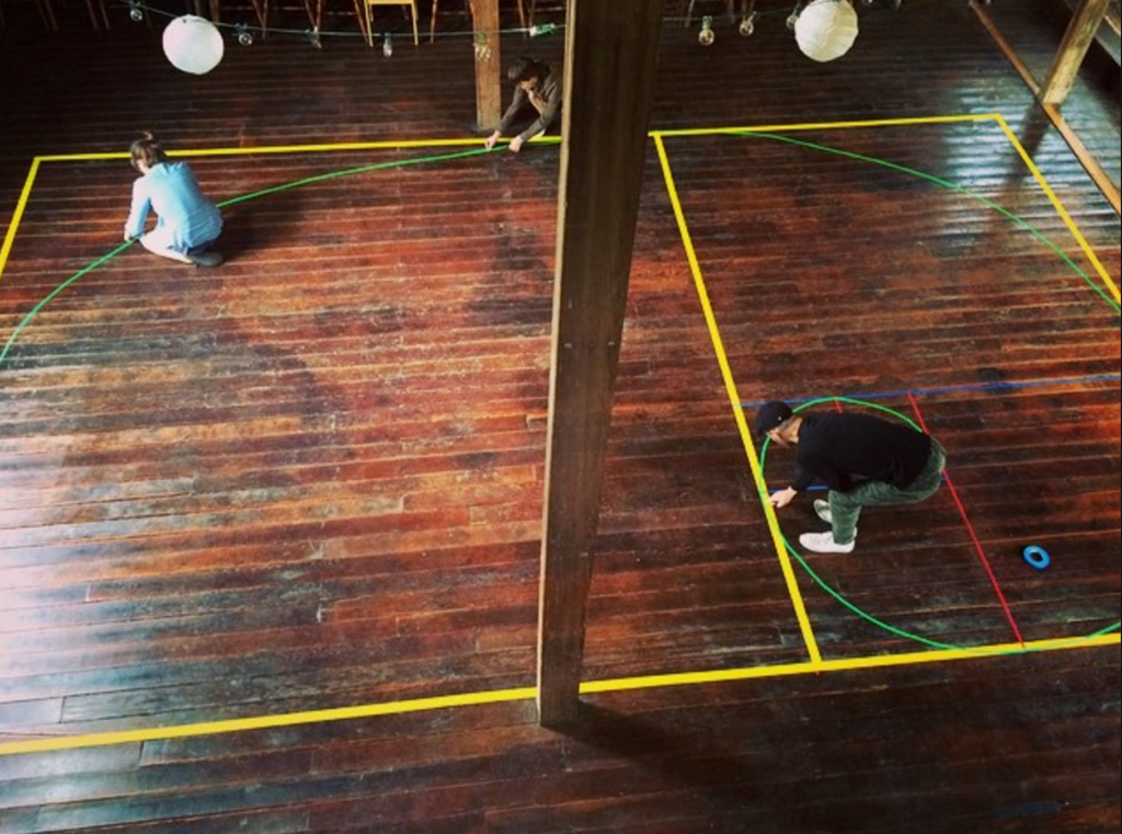 Overhead shot of two people laying down patterned, colored tape on wooden floor.