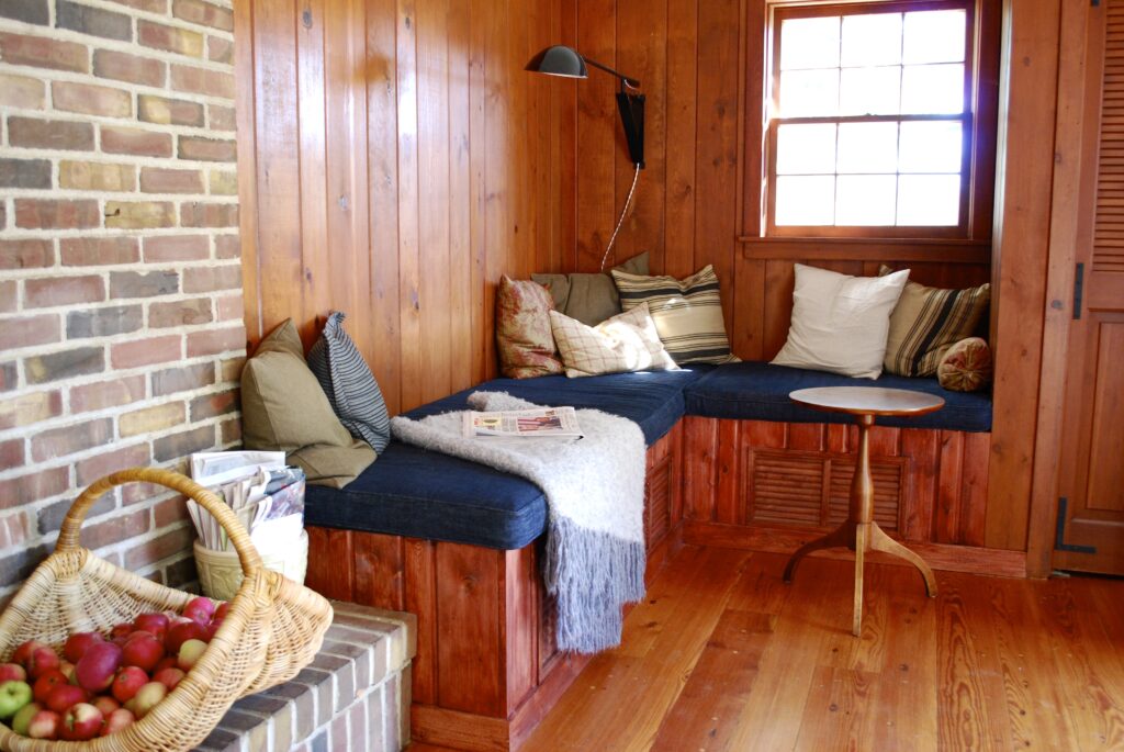 Bench in corner with pillows and blankets, and wooden floor and walls.
