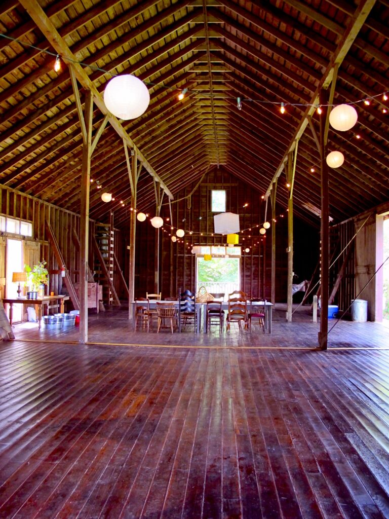Interior of converted barn with wooden floor, walls, and ceiling, and many lights hung from ceiling.