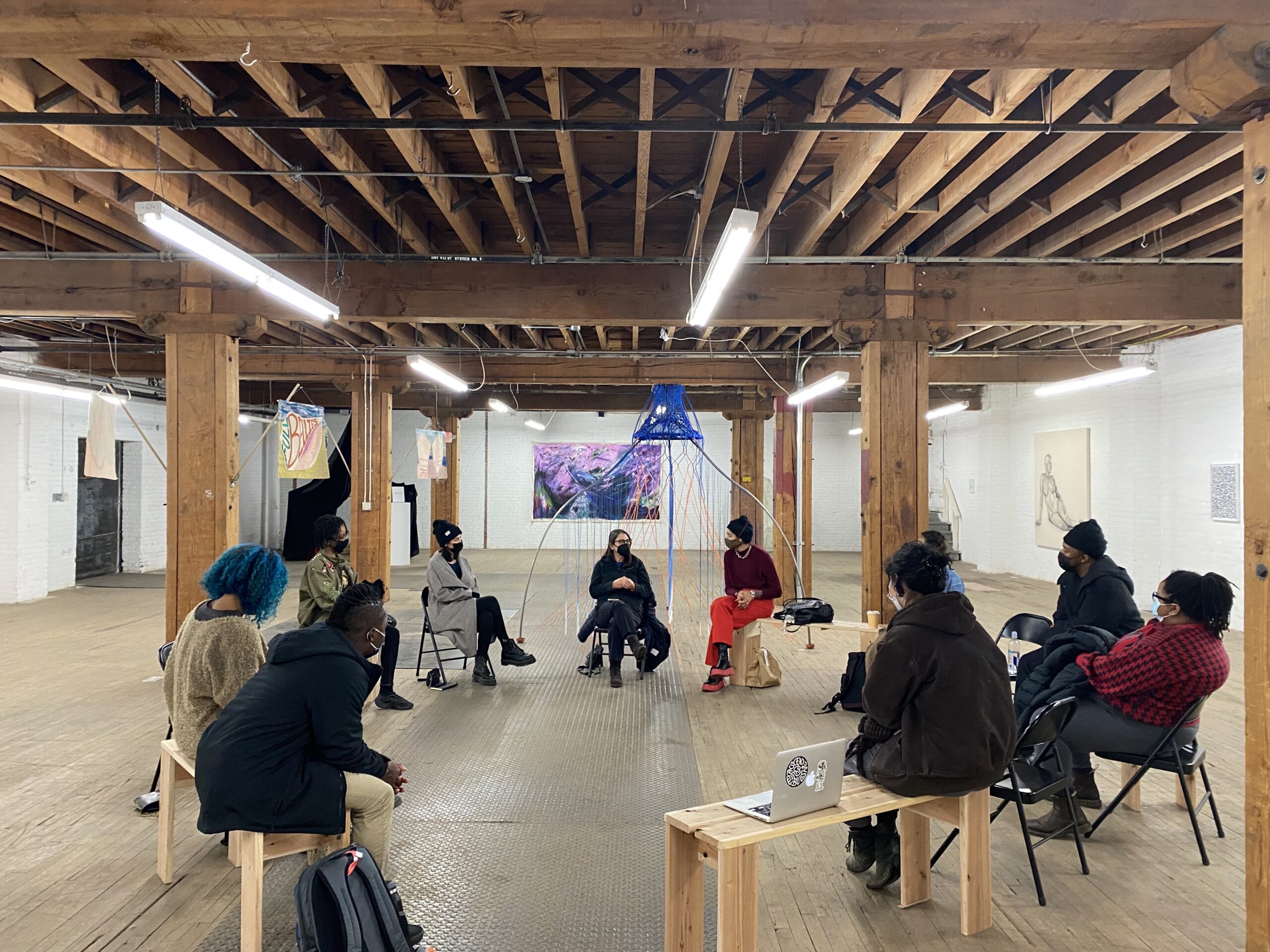 Circle of people in an industrial studio/gallery with artwork throughout.