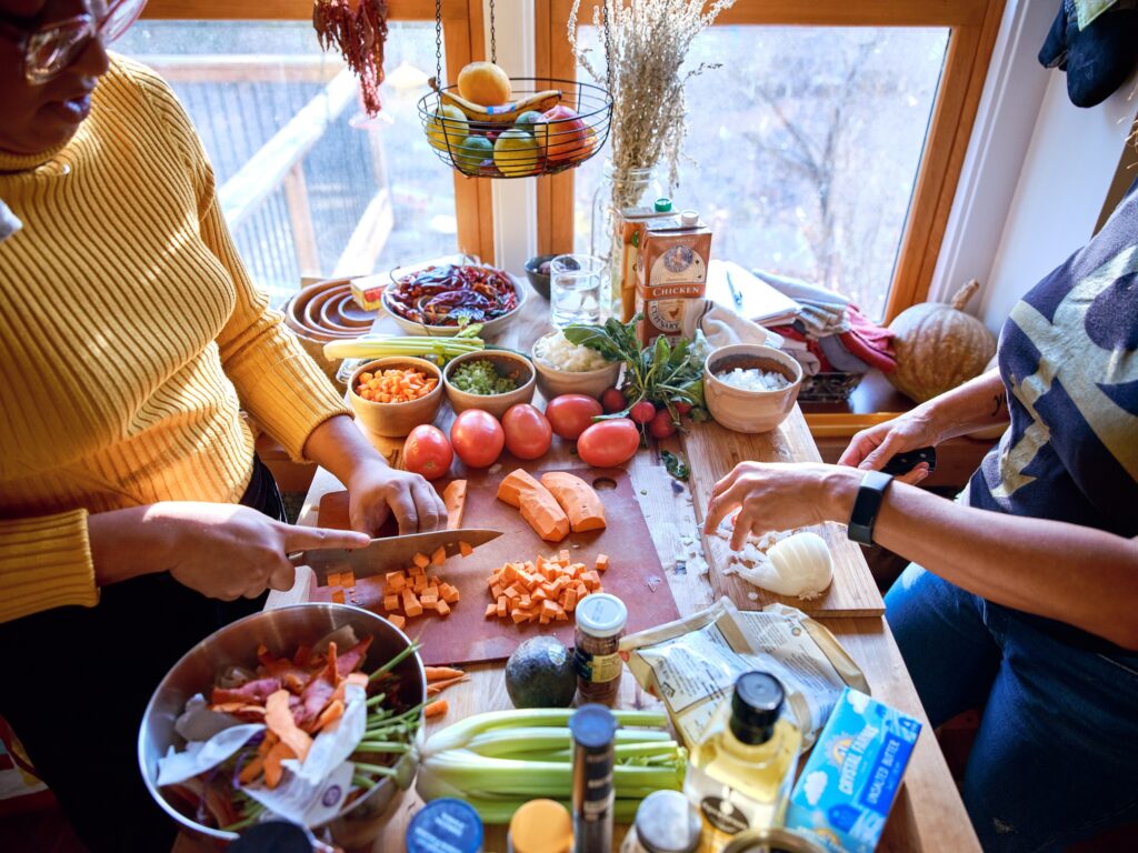 Two sets of hands chop vegetables at kitchen island.