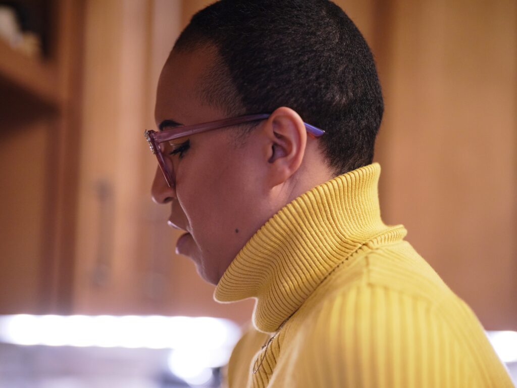 Black woman with yellow turtleneck and pink glasses in profile.