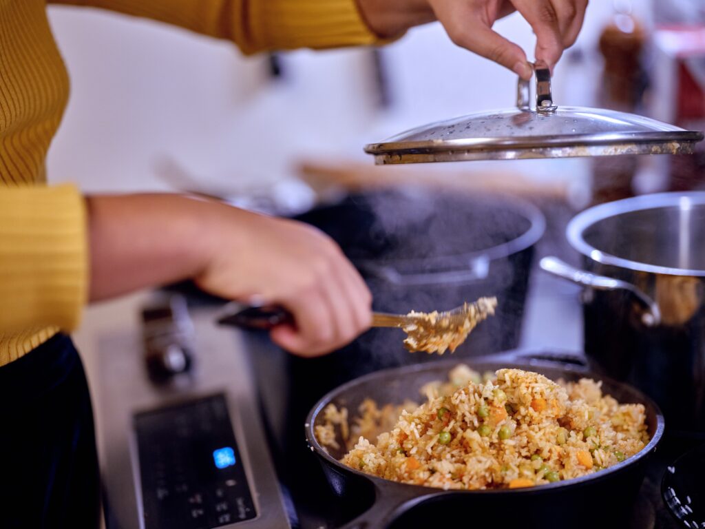 Hands lift pot lit and stir rice.