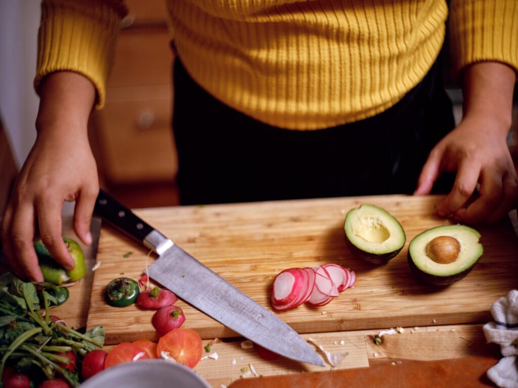 Cutting board with sliced radish, halved avocado, tomatoes, and large knife.
