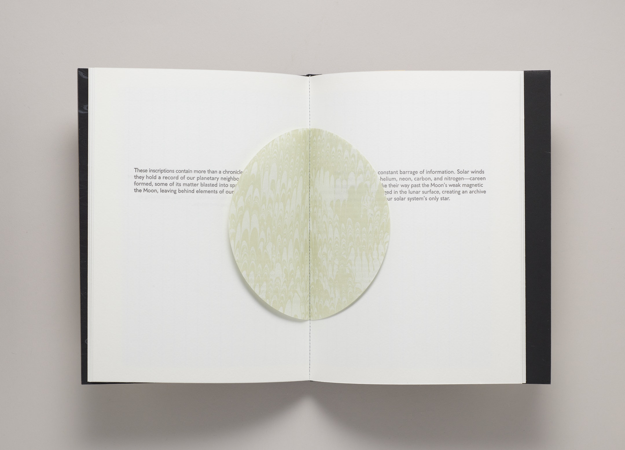 Open book with short black text on white page, overlaid with round moon-like paper form.