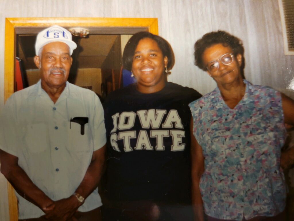 Three people with dark skin stand close and smile for the camera.