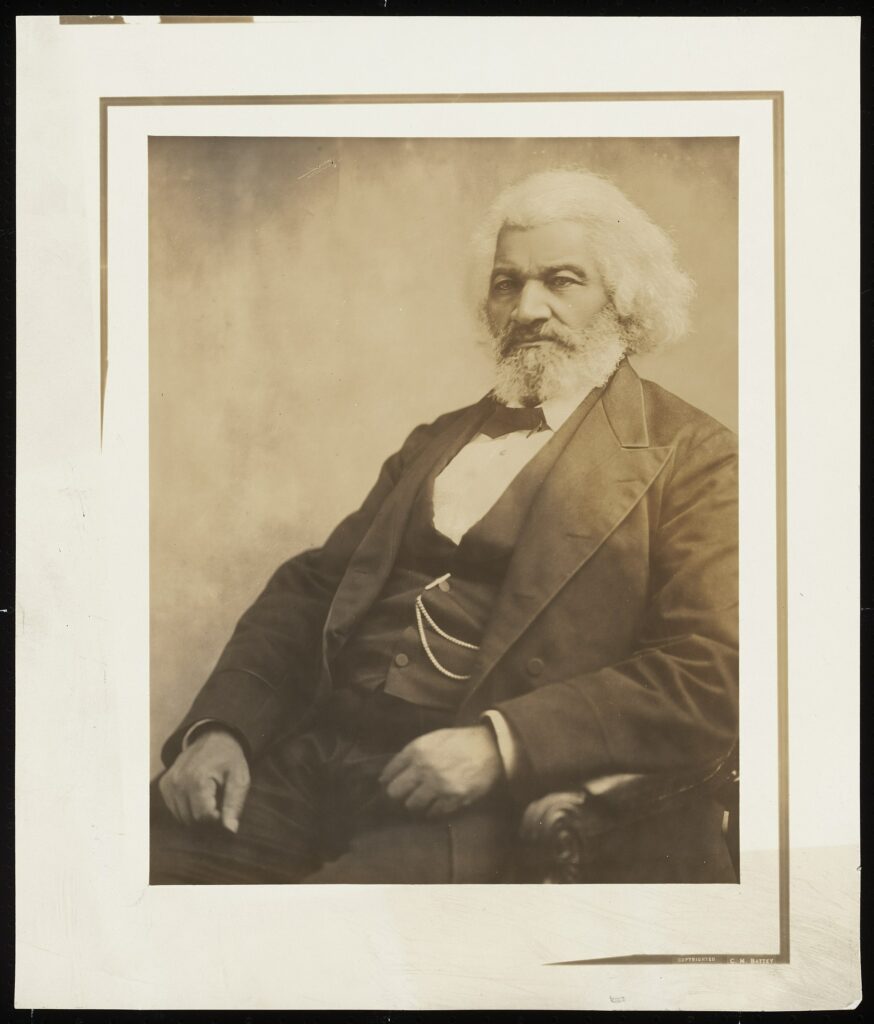 Old sepia photograph of man sitting in suit with white hair and beard.