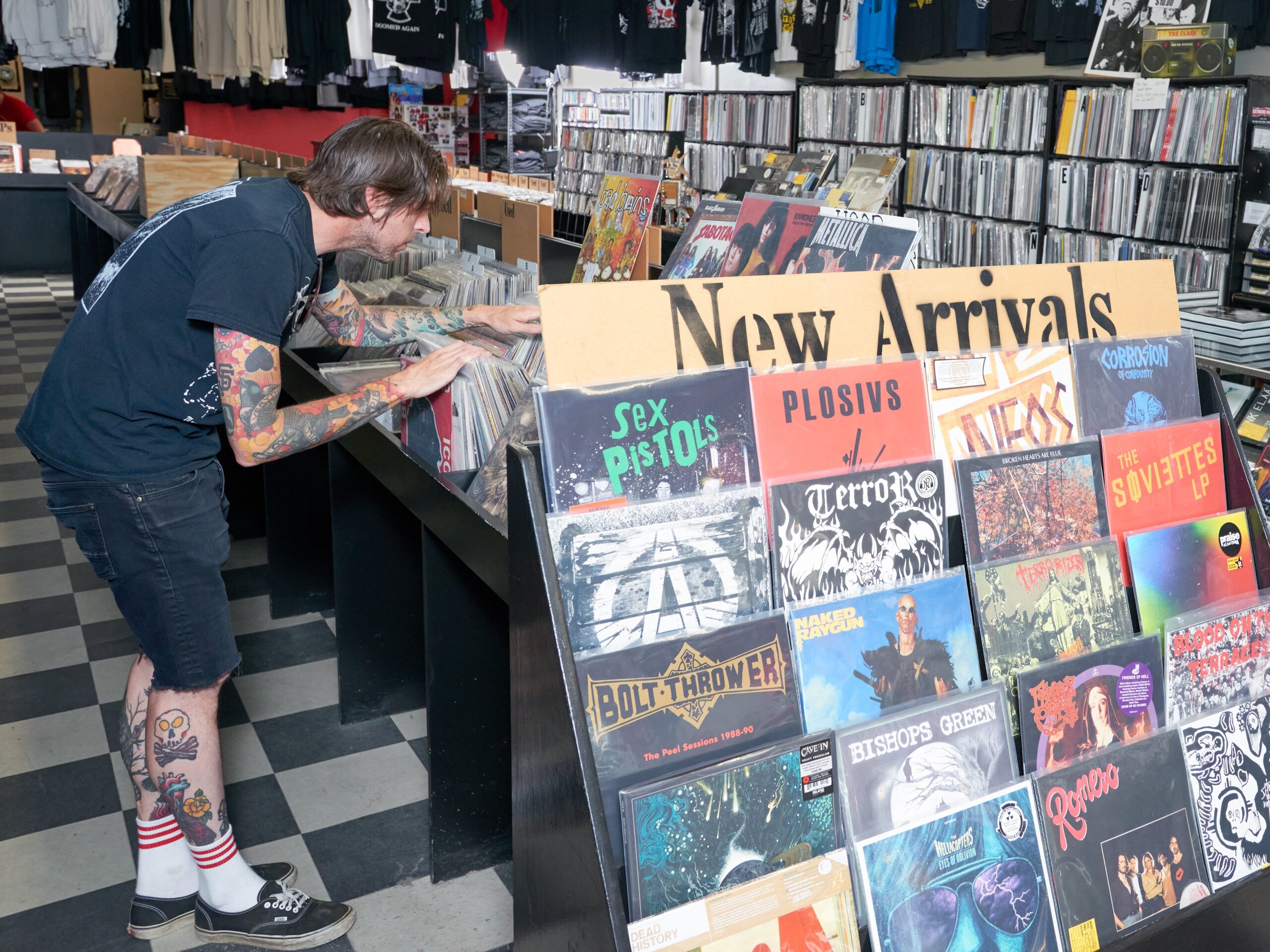 Person leans over to look through a table full of records, with a display reading "New Arrivals" in foreground.