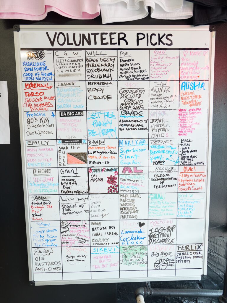 White board with title VOLUNTEER PICKS and writing in grid in multicolored markers.