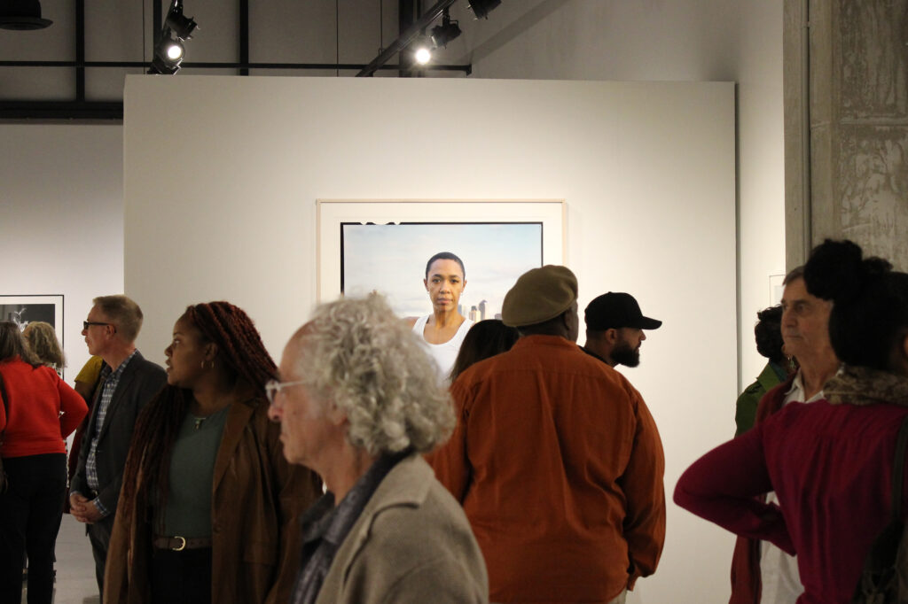 People mingling in gallery with a portrait photograph hung in background
