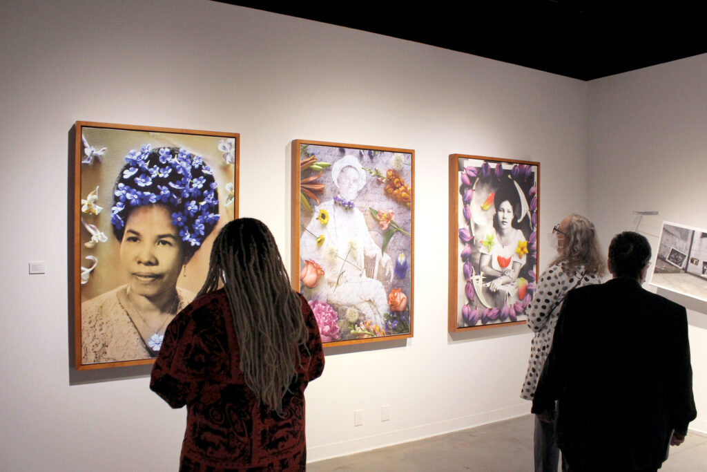 People standing in gallery in front of three large photographs with colorful flowers on black and white portraits