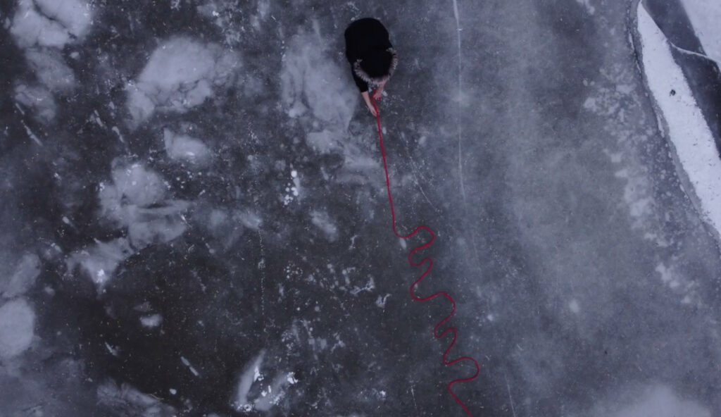 Aerial of a person on ice holding a bright pink rope