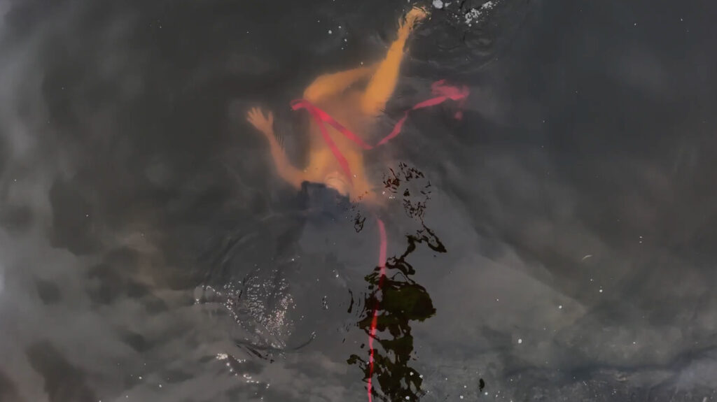 Aerial view of naked person with bright pink rope submerged in dark water