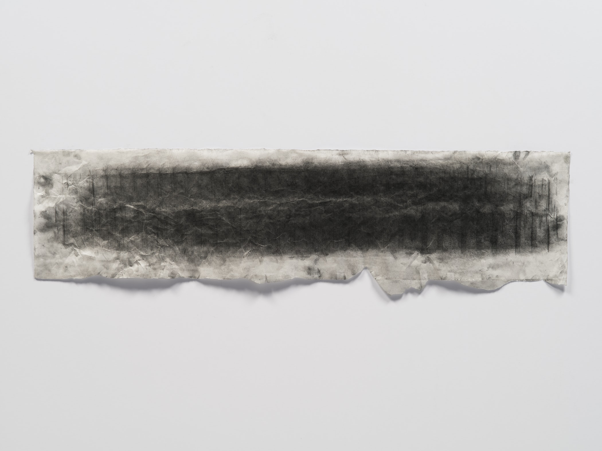 Long, rough paper with solid dark markings hung horizontally on white wall.