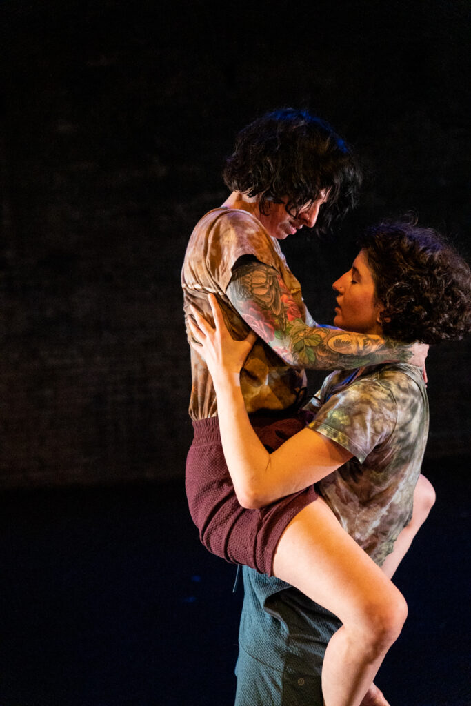 Two dancers with light skin and curly hair, one with legs wrapped around the other's waist.