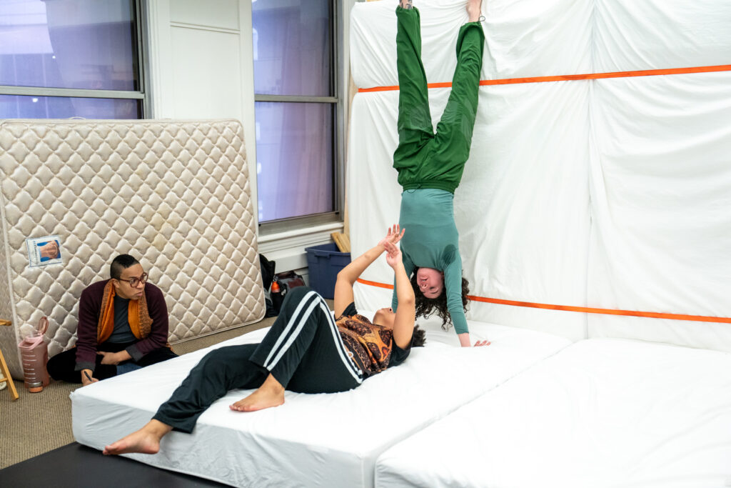 Two dancers on set made of mattresses, one in handstand and the other on her hand, with third person sitting to the side.