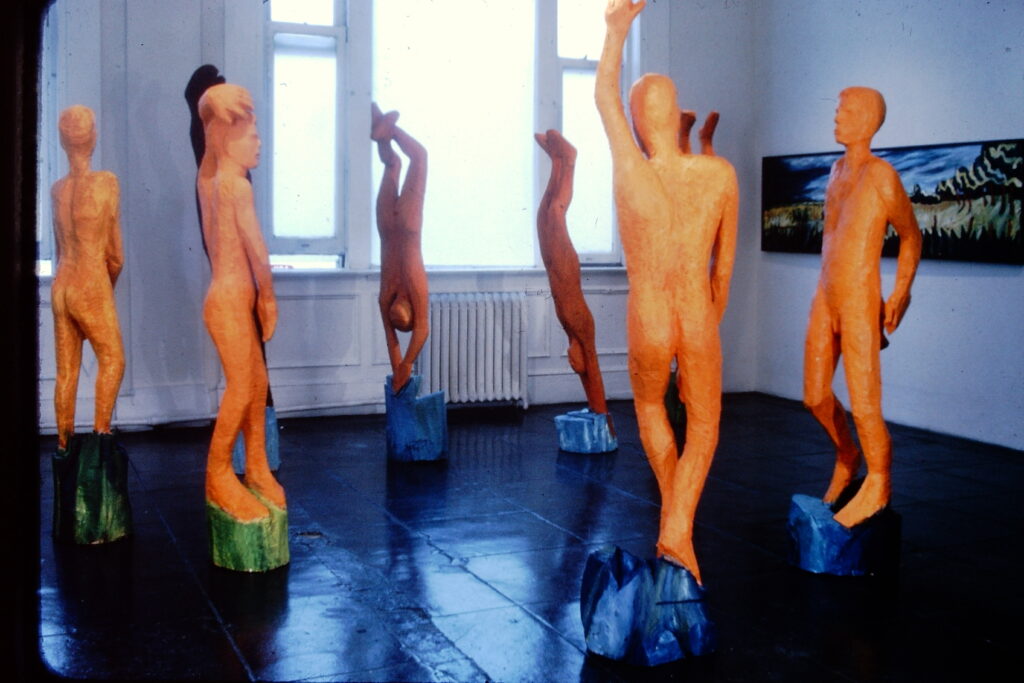Grouping of six sculptures with human forms, painted orange.