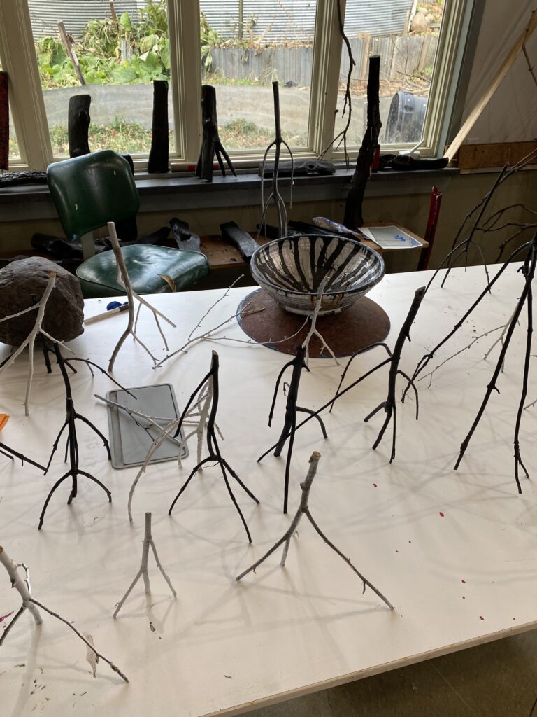 Many small sculptures made of tree branches standing up on table.