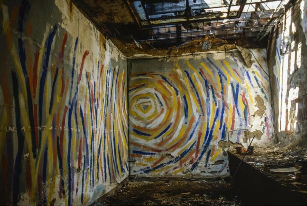 Painting in yellow, orange, and blue circular forms covers two walls of industrial building.