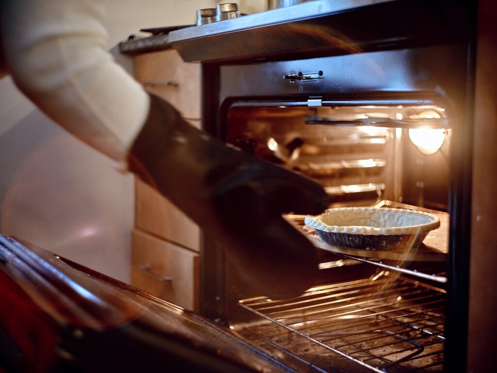Hand with oven mitt reaches into oven towards empty pie crust.